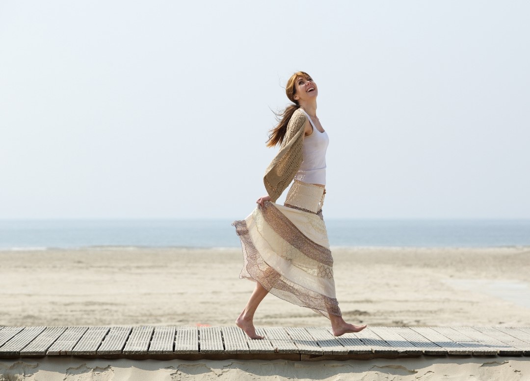 Woman walking happily and carefree looking along a beach path