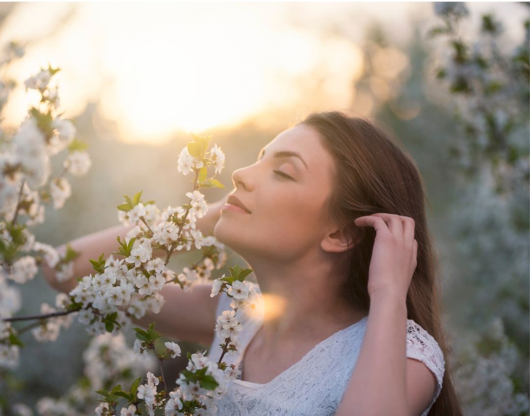 Awakened woman enjoying being present and smelling flowers with bright sunlight behind her